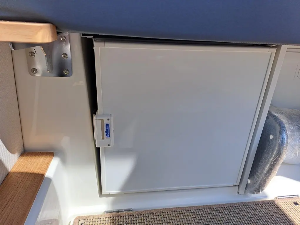 White marine refrigerator installed in a boat with a wooden shelf and a wrapped item in the background.